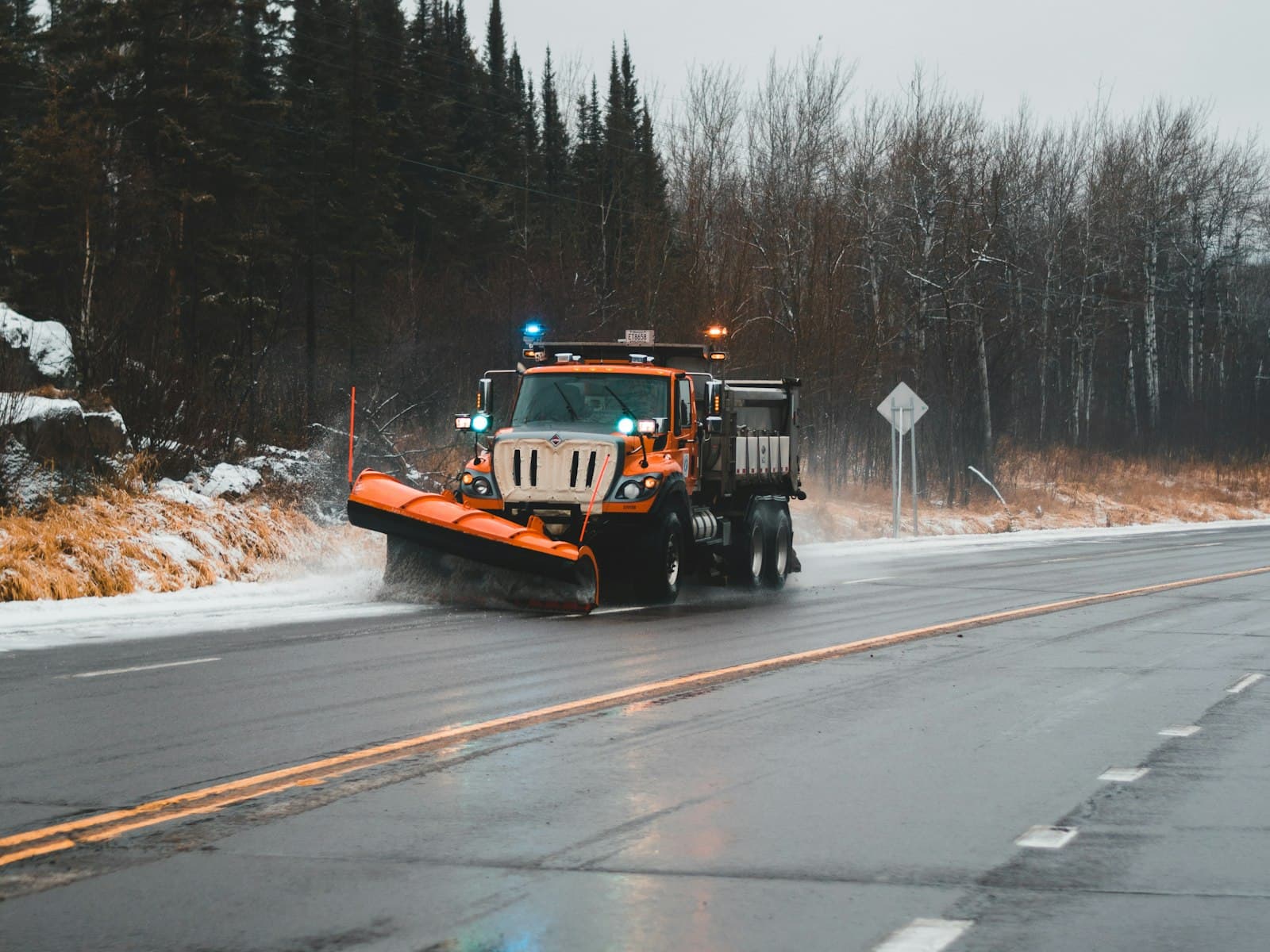 A commercial snow plow truck clearing and salting a parking lot during a Michigan winter storm